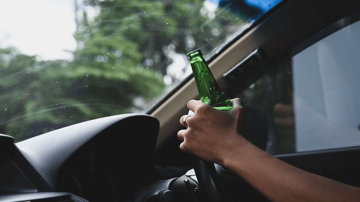 Un conductor con una botella de cerveza en la mano mientras sujeta el volante