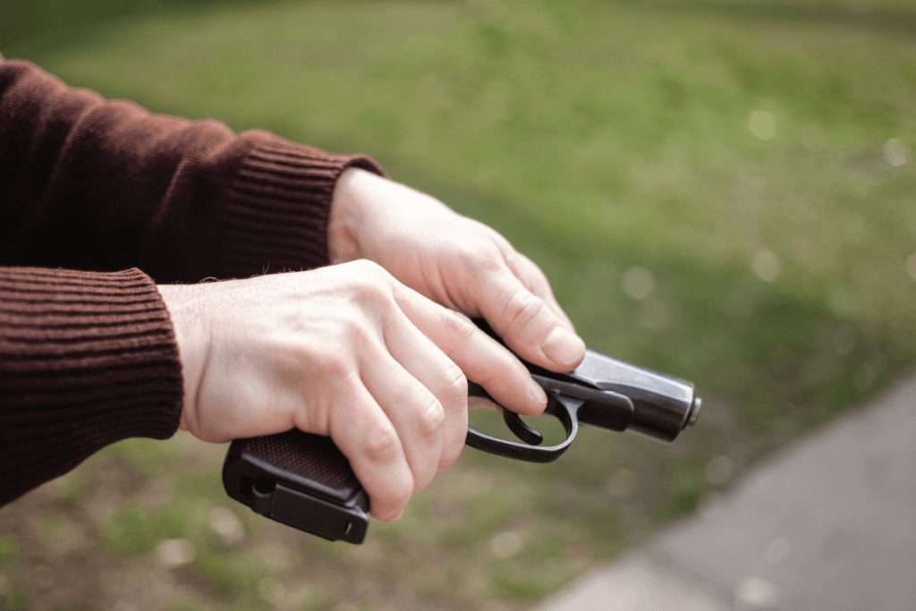 Una mano que sostiene una pistola apuntando al suelo al aire libre