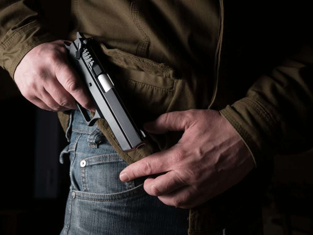 Un hombre metiéndose una pistola en la cintura de los jeans