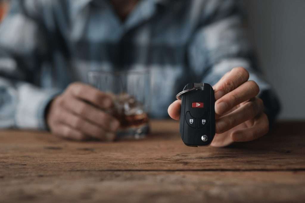 Un hombre con las llaves del coche en la mano junto a un vaso de whisky