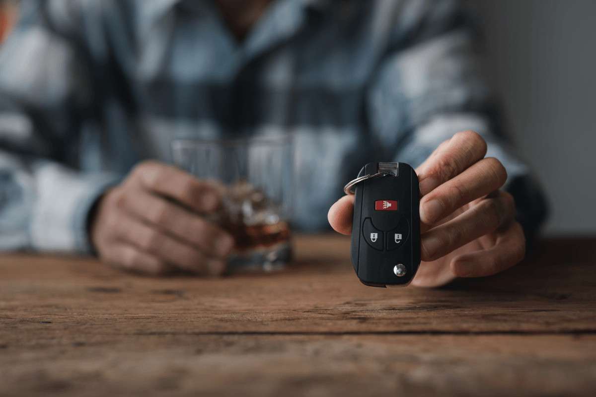 Un hombre con las llaves del coche en la mano junto a un vaso de whisky