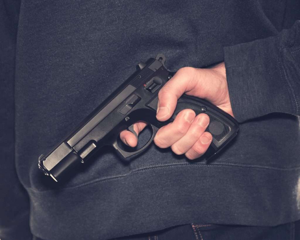 Una mano sacando una pistola de detrás de la espalda de un hombre