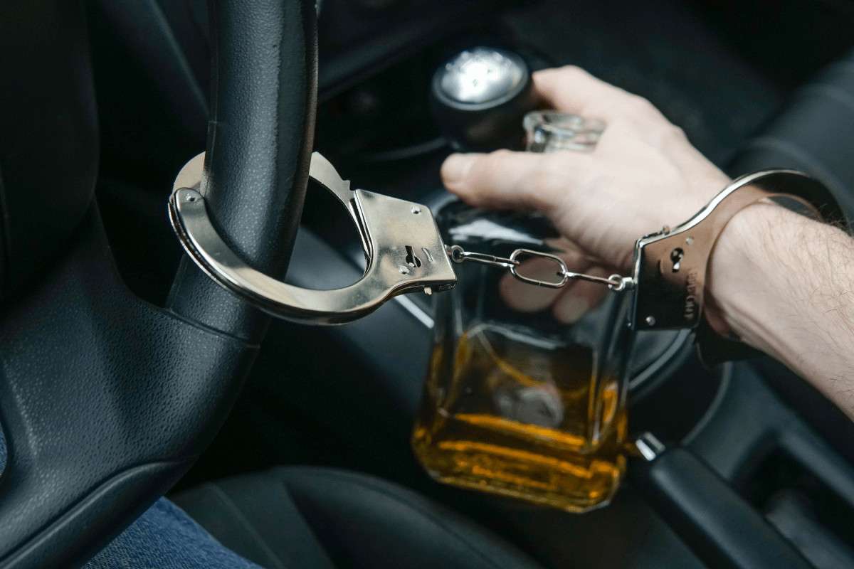 La muñeca de un conductor esposada al volante junto a un vaso de whisky