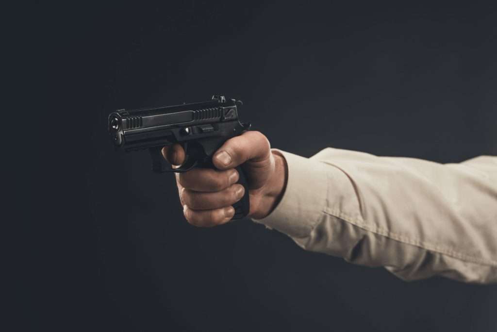 Un brazo apuntando con una pistola sobre un fondo oscuro