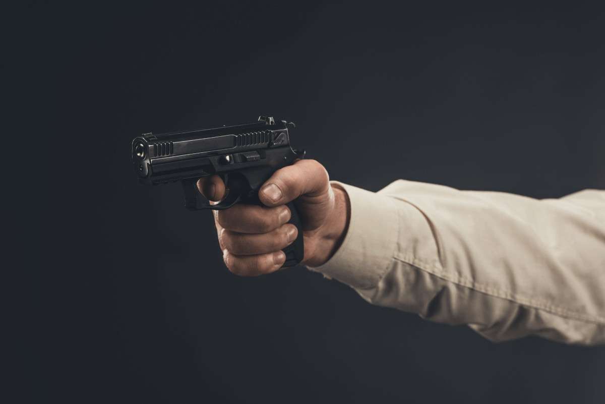 Un brazo apuntando con una pistola sobre un fondo oscuro
