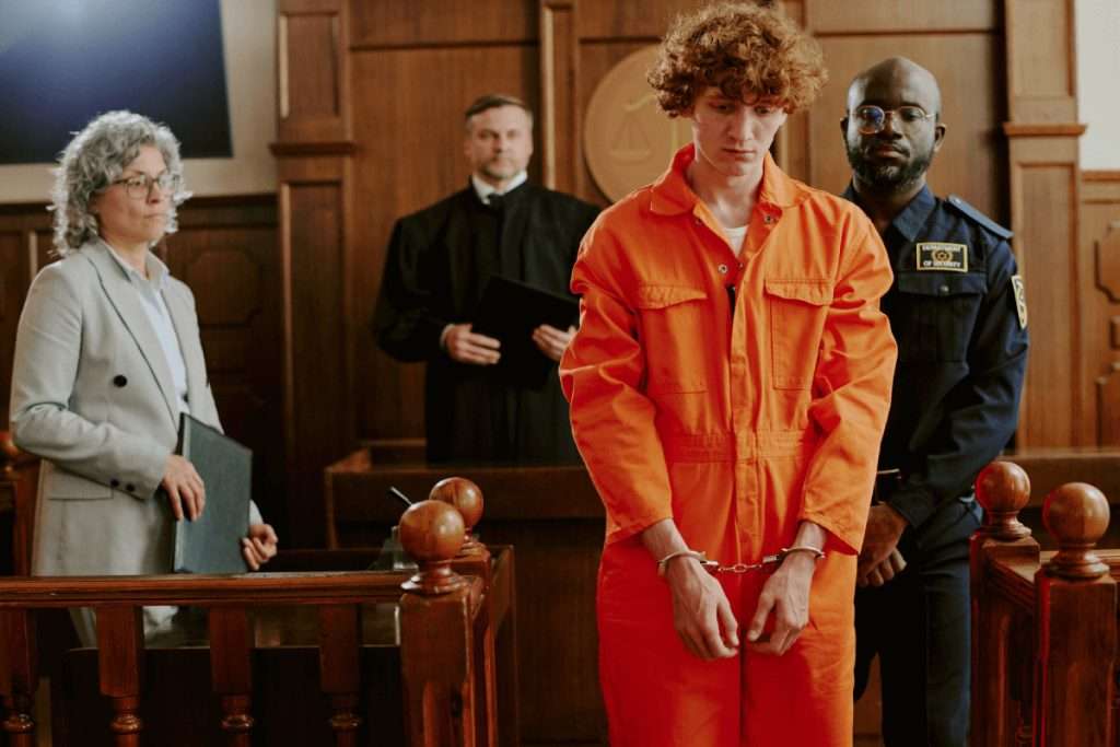 Un joven con un mono naranja y esposas de pie en una sala de tribunal