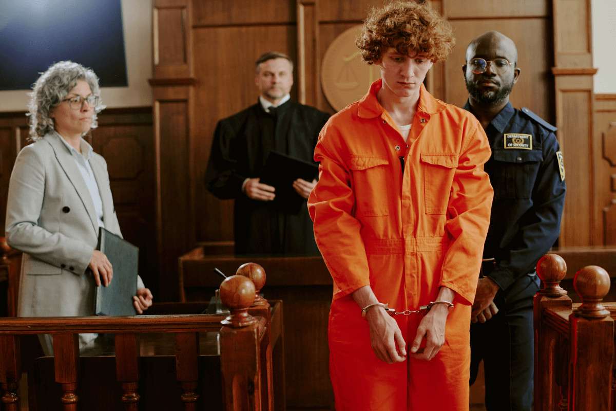 Un joven con un mono naranja y esposas de pie en una sala de tribunal