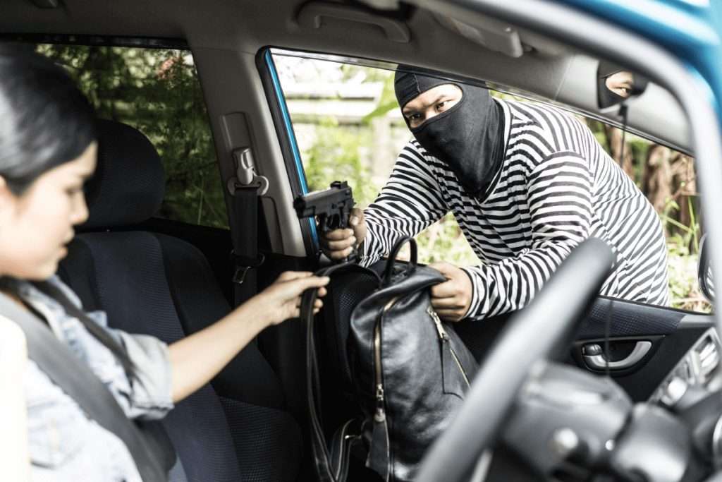 Un hombre enmascarado arrebatando el bolso a una mujer por la ventanilla de un coche