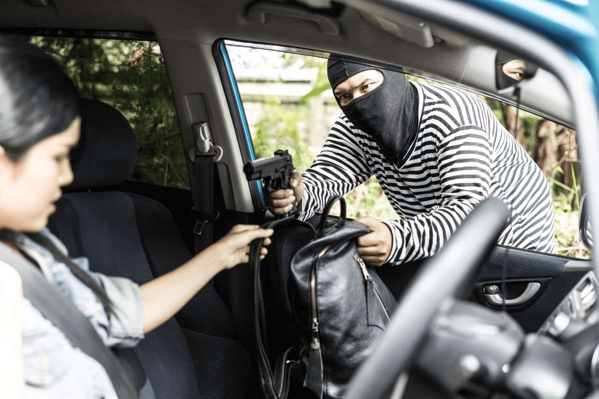 Un hombre enmascarado arrebatando el bolso a una mujer por la ventanilla de un coche