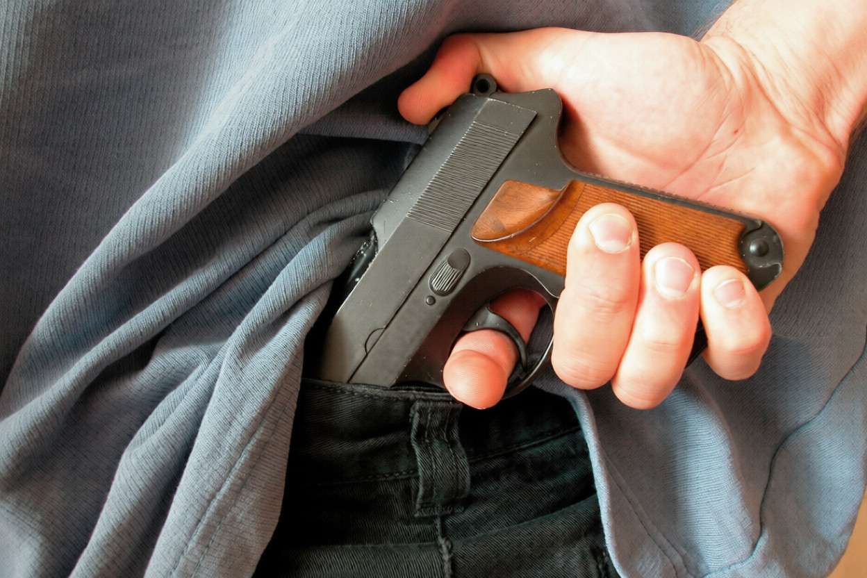 Un hombre sacando una pistola de debajo de la camisa