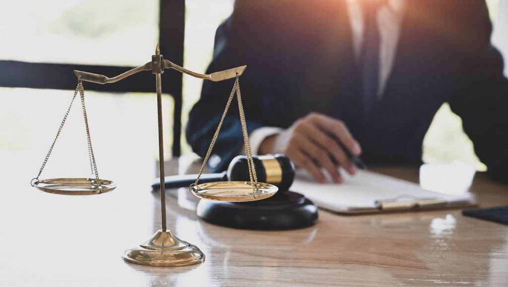 Un abogado escribiendo en un escritorio junto a una balanza de la justicia y un mazo