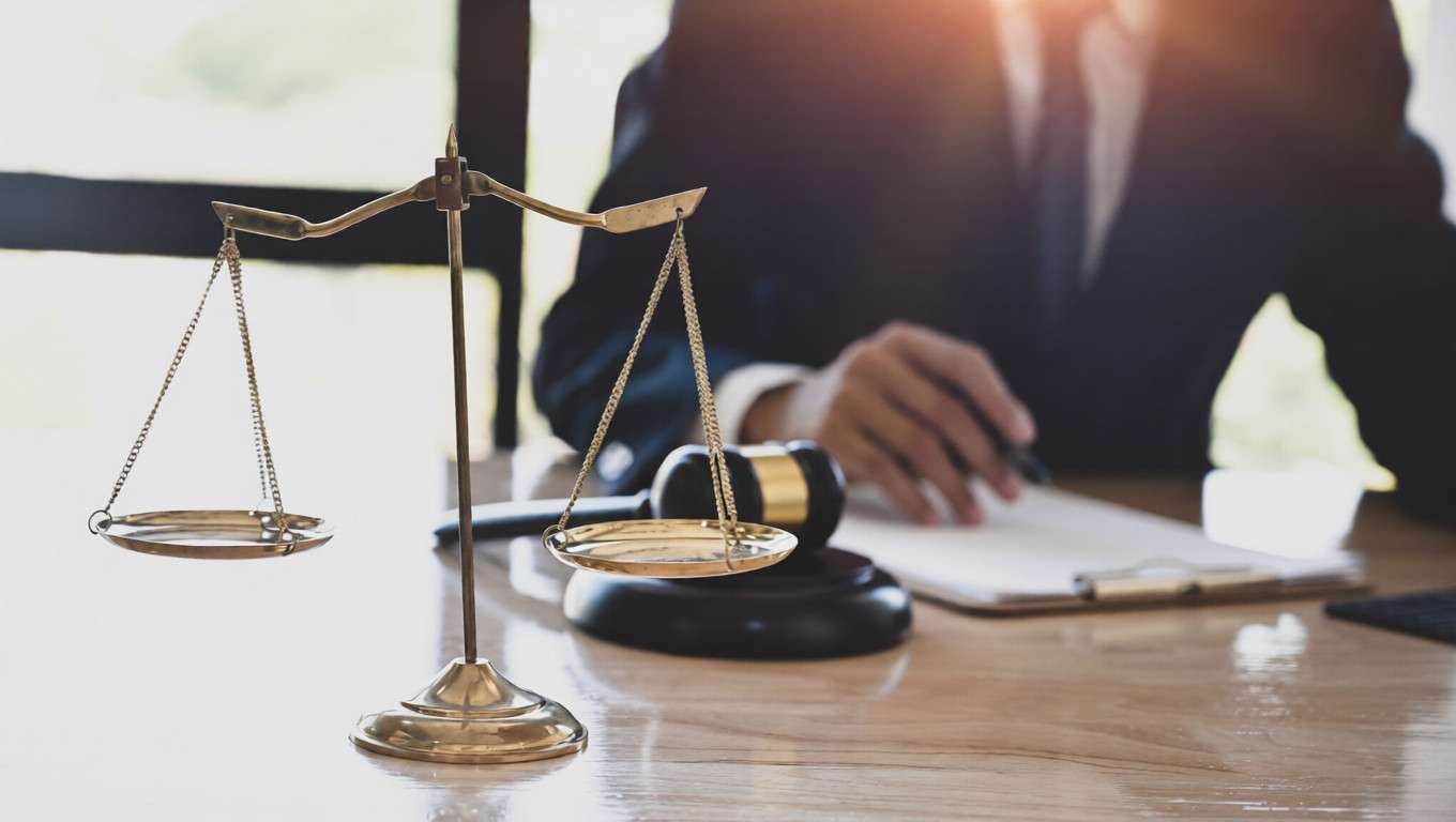 Un abogado escribiendo en un escritorio junto a una balanza de la justicia y un mazo