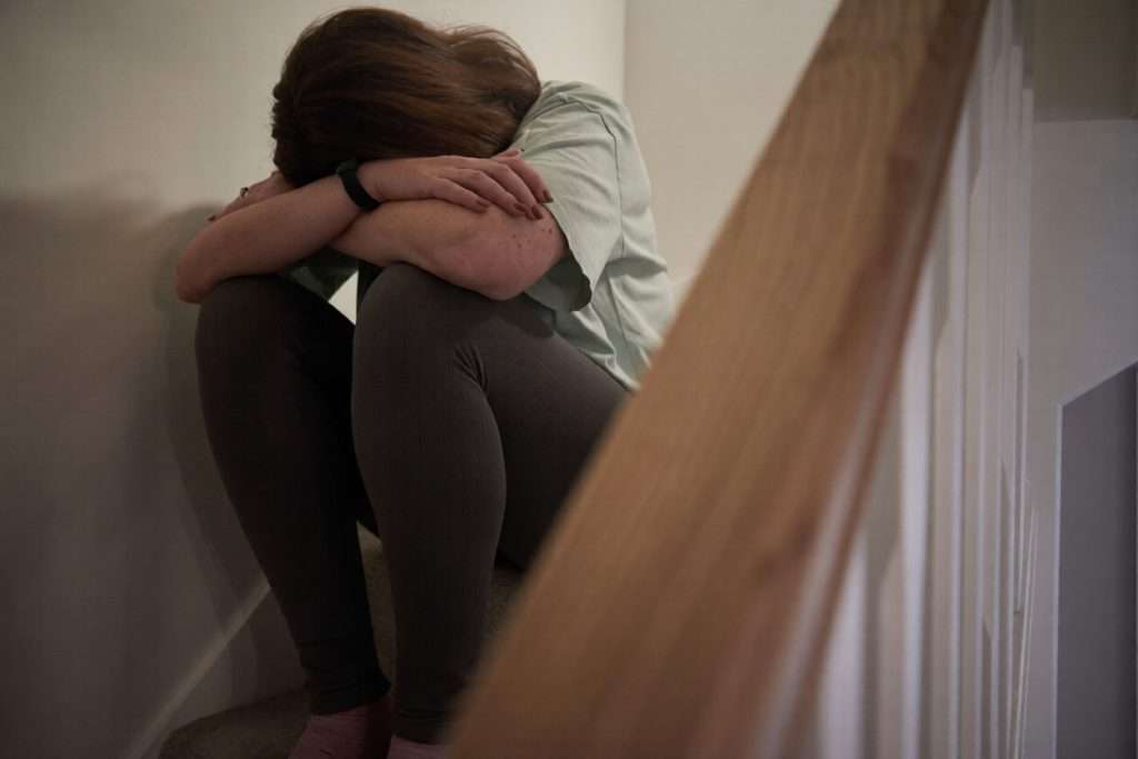 Una mujer sentada en el suelo con la cara escondida entre los brazos