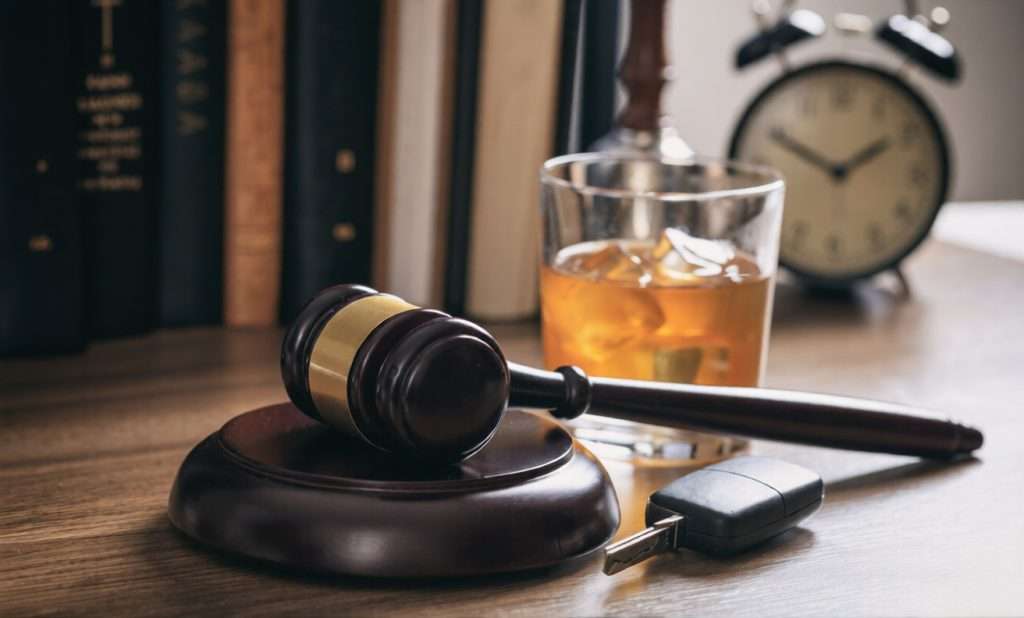 Un mazo, las llaves de un coche y un vaso de whisky sobre un escritorio