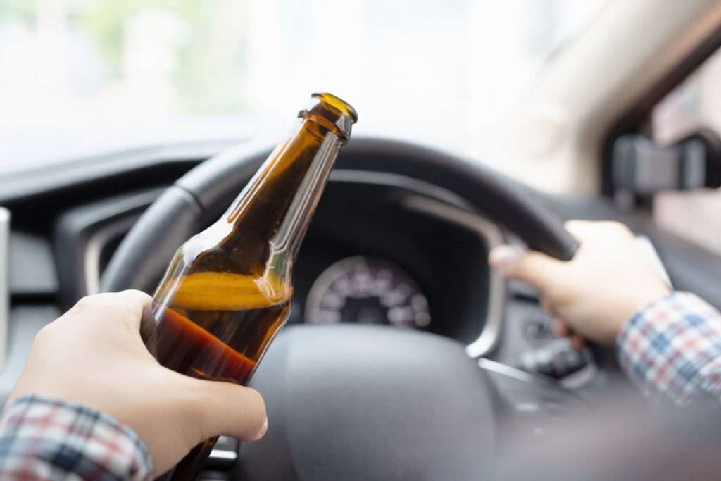 Un conductor con una botella de cerveza en la mano mientras conduce