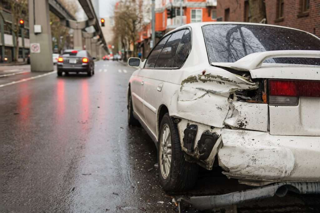 Un coche blanco dañado detenido en una calle mojada de la ciudad