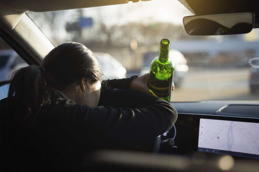 Una mujer desplomada sobre el volante con una botella en la mano