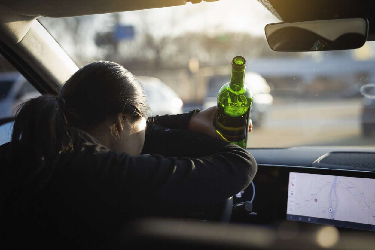 Una mujer desplomada sobre el volante con una botella en la mano