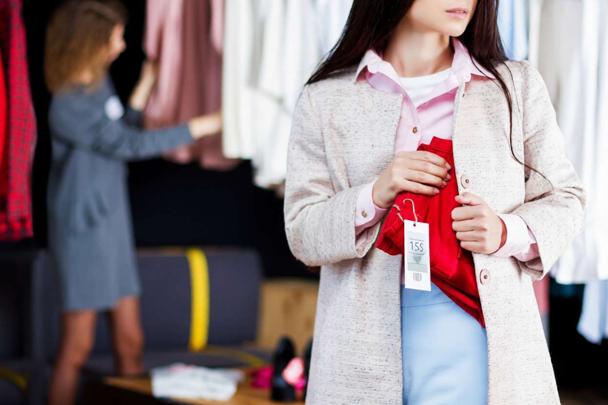 Una mujer escondiendo una camisa roja bajo el abrigo en una tienda de ropa